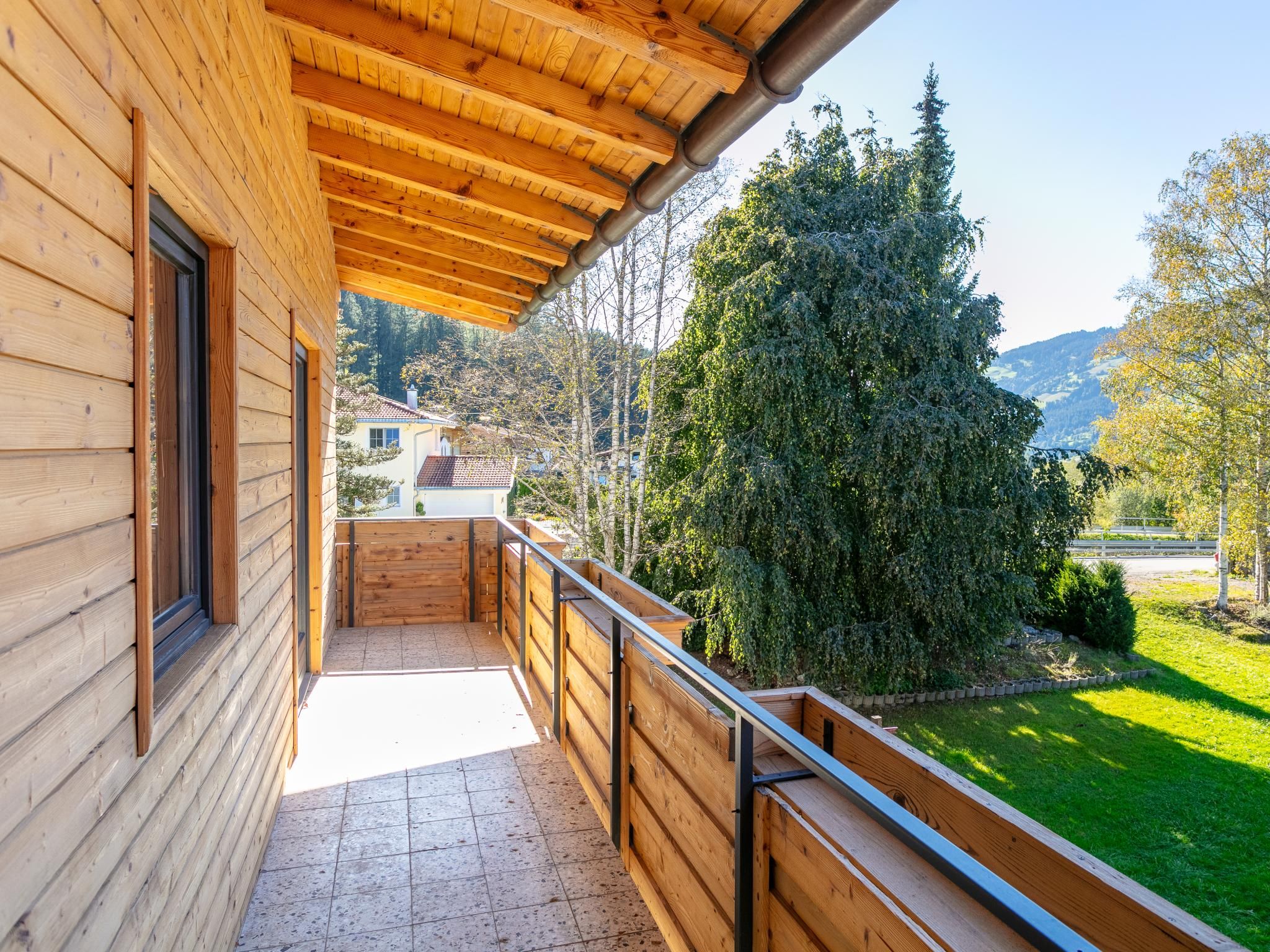A wooden balcony with a view of a green landscape and trees.