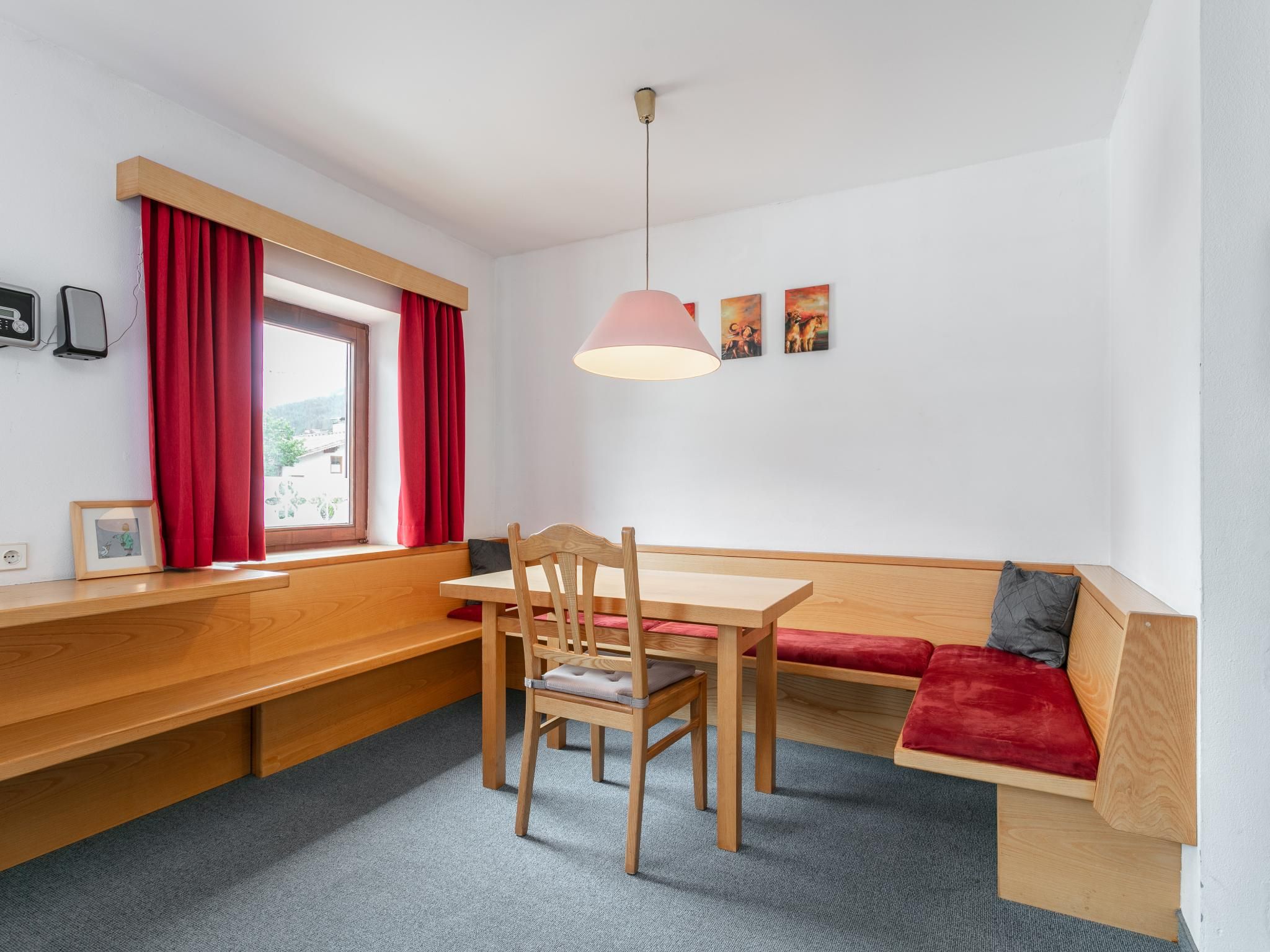 A room with a wooden bench, a table, a chair, a red sofa, and a hanging light fixture.