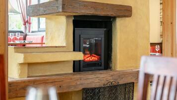 A fireplace with a fire burning inside, set in a yellow wall with a wooden beam above it.