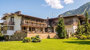 A two-story building with balconies, a stone facade, and a mountainous backdrop.
