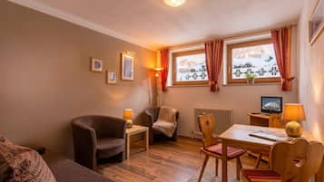 A cozy room with a sofa, two chairs, a table, a lamp, a radiator, and a window with a view of mountains.