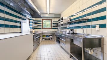 A commercial kitchen with stainless steel appliances, a window with a view of trees, and tiled walls.