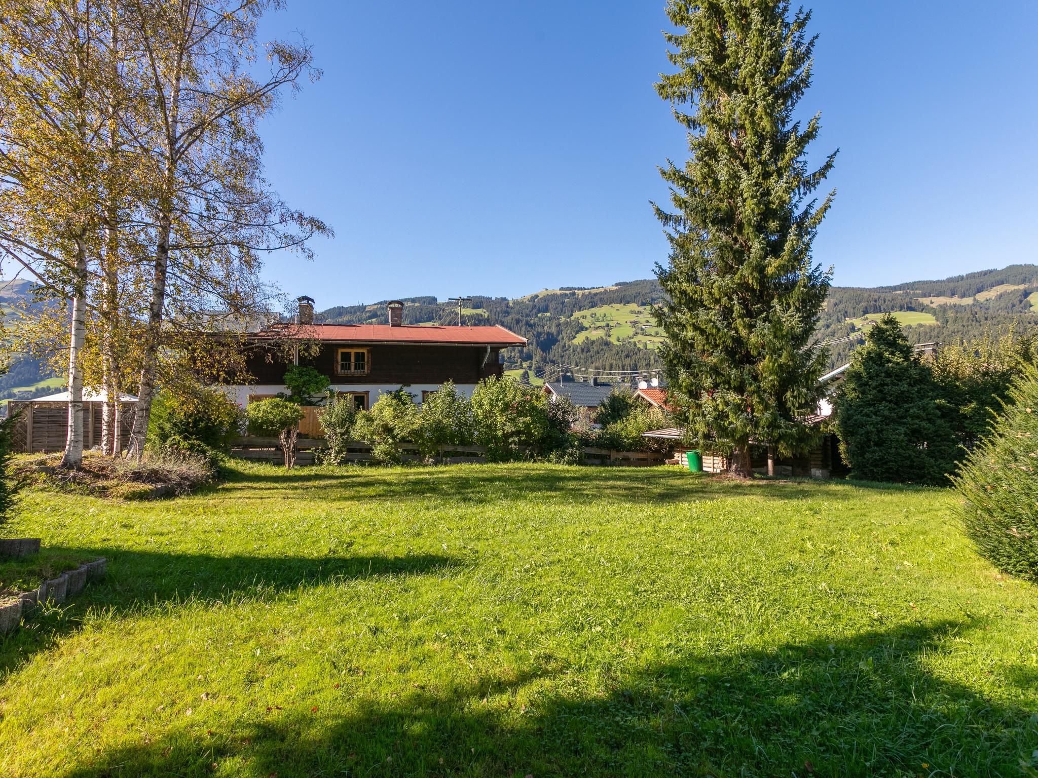 Ein Haus mit rotem Dach, umgeben von einem grünen Rasen und Bäumen.