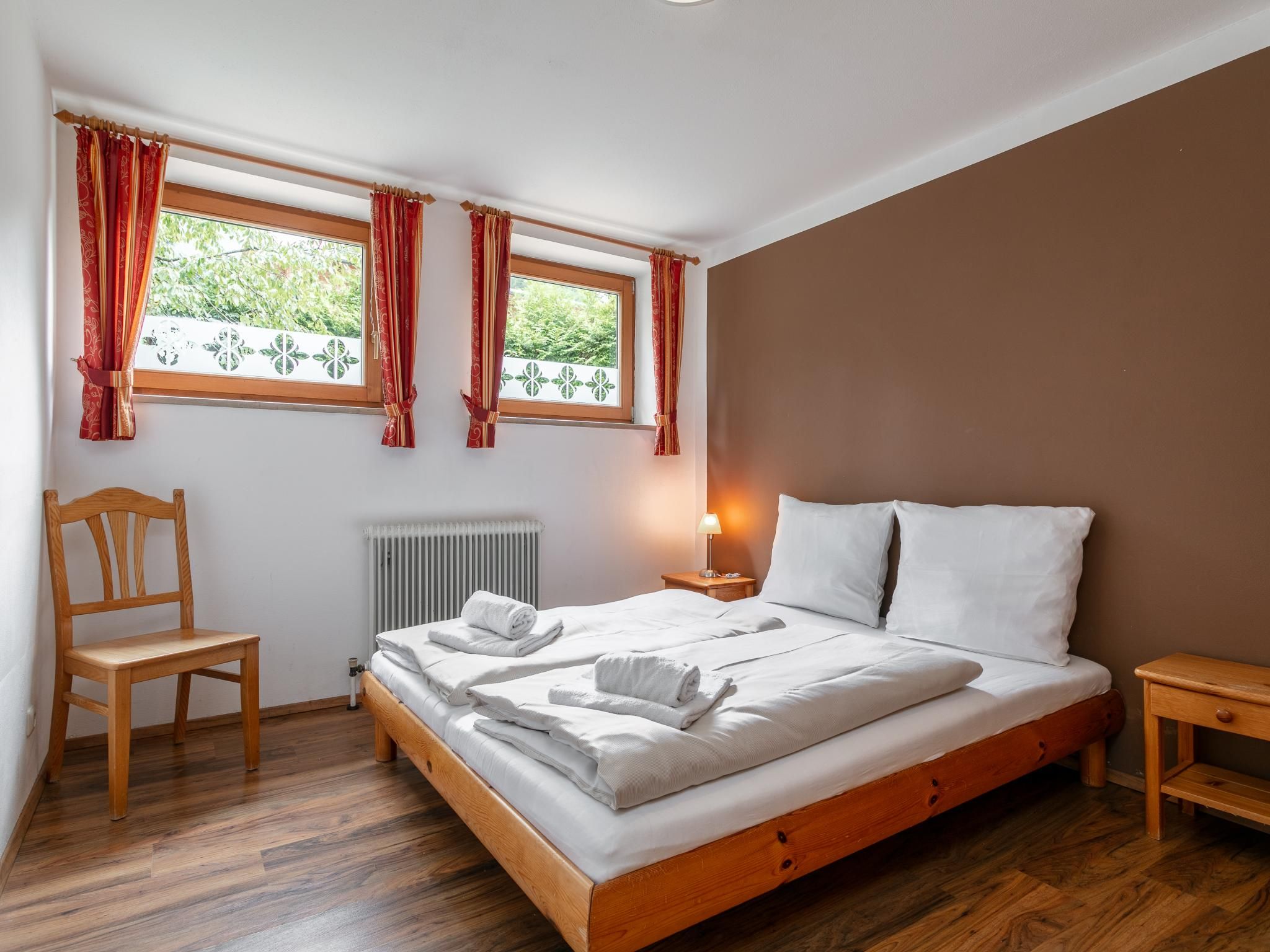 A bedroom with a wooden bed, a chair, a bedside table, and a window with curtains.