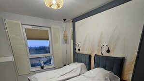Un dormitorio con dos camas, una ventana con contraventanas, una lámpara colgante y vistas al exterior.