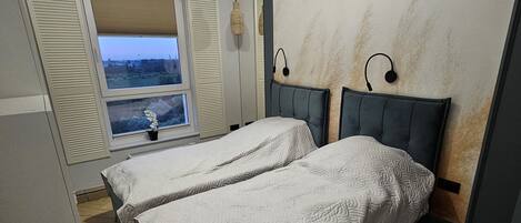 Un dormitorio con dos camas, una ventana con contraventanas, una lámpara colgante y vistas al exterior.