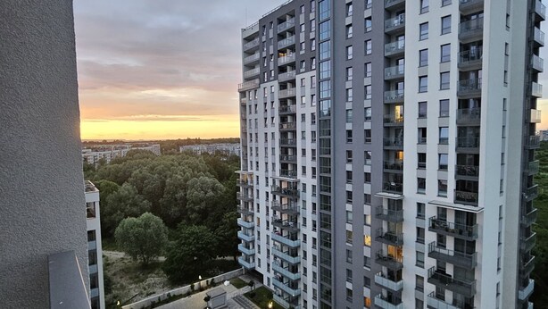 Un edificio residencial alto con varios balcones, un área de estacionamiento y vistas al atardecer.
