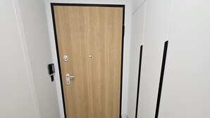Un pasillo con una puerta de madera, una pared blanca, un suelo con diseño de espiga y un par de zapatos sobre una alfombra.