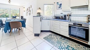 Een moderne keuken met witte kasten, een inbouwoven en een eethoek met een blauwe tafelkleed.