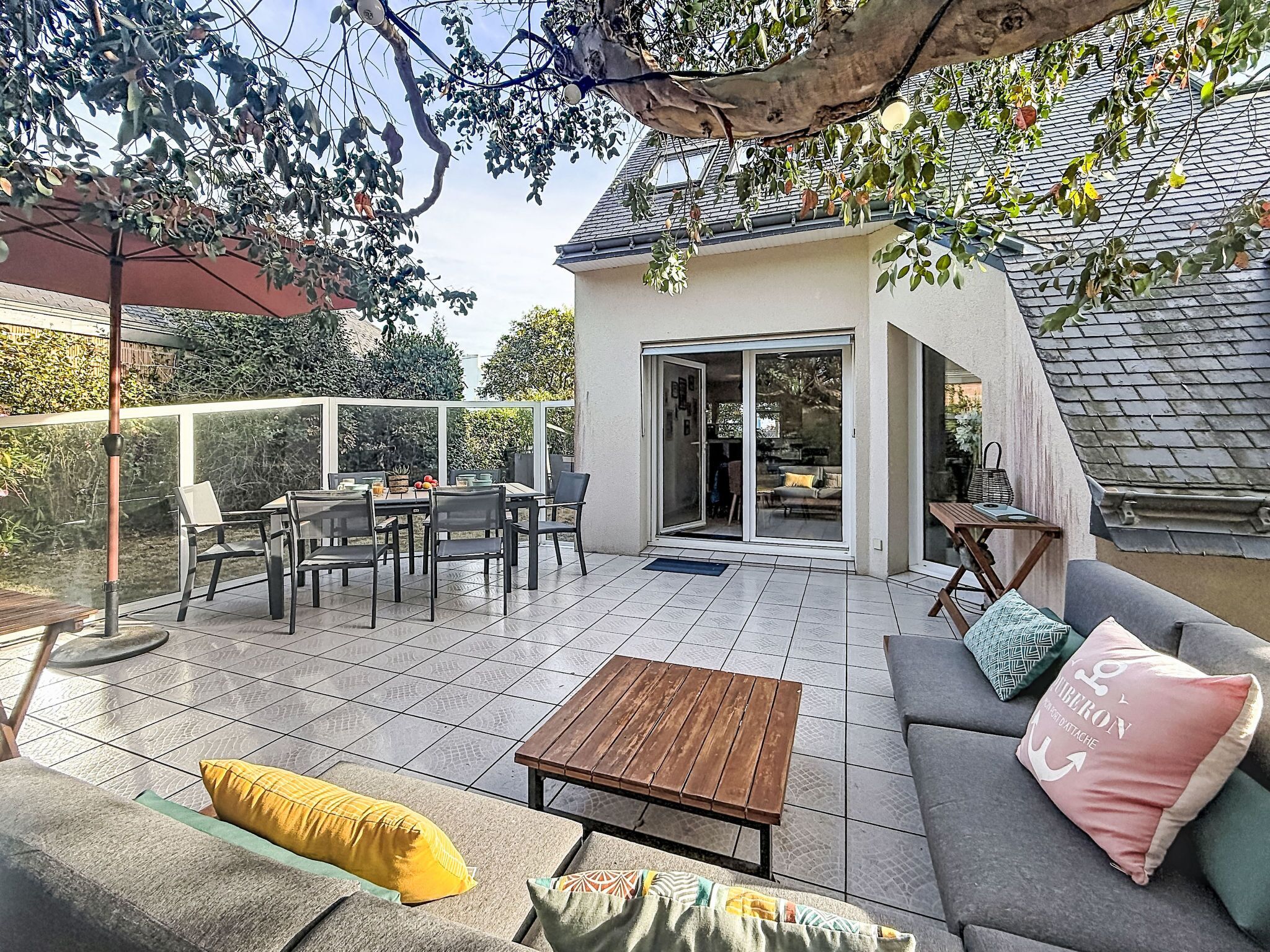 Eine überdachte Terrasse mit Esstisch und Stühlen, einer Couch mit Kissen sowie einem Holztisch.