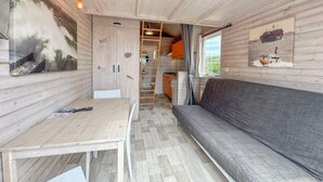 A compact interior with a sofa, table, kitchen area, and a ladder leading to a loft. - Fully equipped beach house with a terrace (Ellemeet)