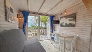 A cozy cabin interior with a sofa, a dining table, chairs, a TV, and a large window with curtains. - Fully equipped beach house with a terrace (Ellemeet)