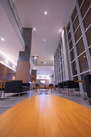 Een ruime lobby met een houten vloer, moderne zitplaatsen en grote ramen.