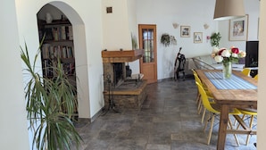 A room with a fireplace, a wooden table with chairs, a bookshelf, and a door leading to another room. - Large family home in the middle of an olive grove (Le Pradet)
