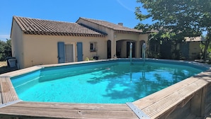 A swimming pool with a wooden deck, a house with a tiled roof, and a tree. - Large family home in the middle of an olive grove (Le Pradet)
