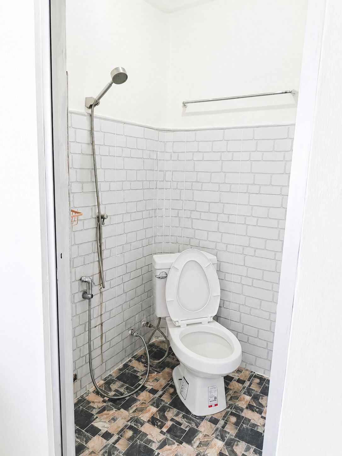 A small, white-tiled bathroom with a shower, toilet, and a towel rack.