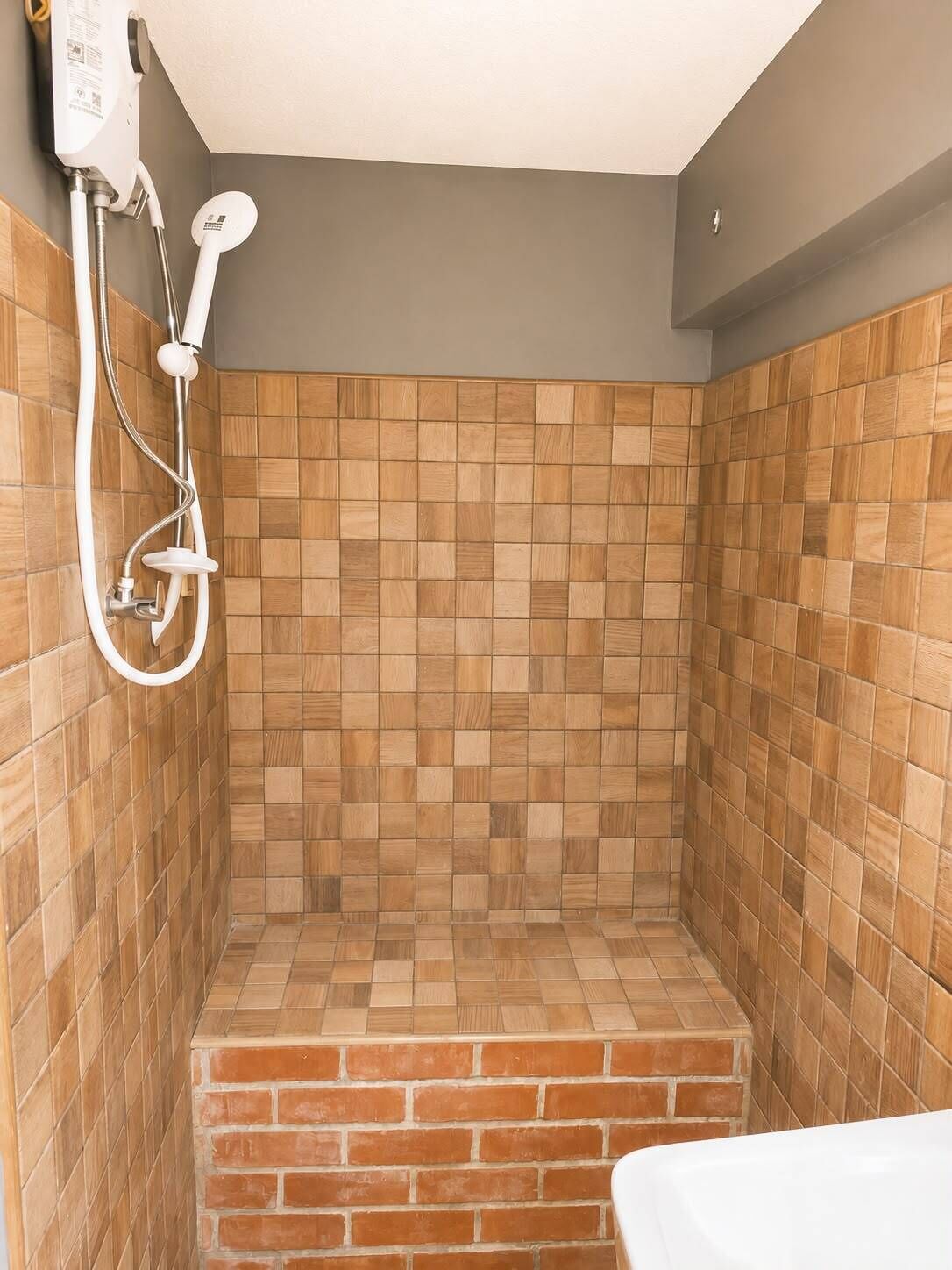 A shower with a tiled wall, a handheld showerhead, and a step leading up to the shower area.