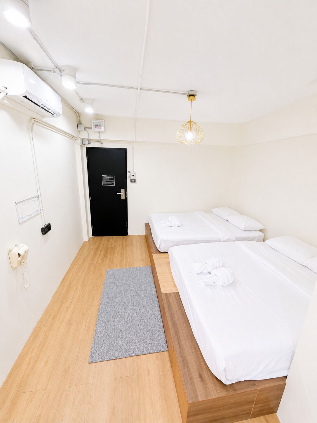 A hotel room with two beds, a grey rug, a black door, and a phone on the wall.