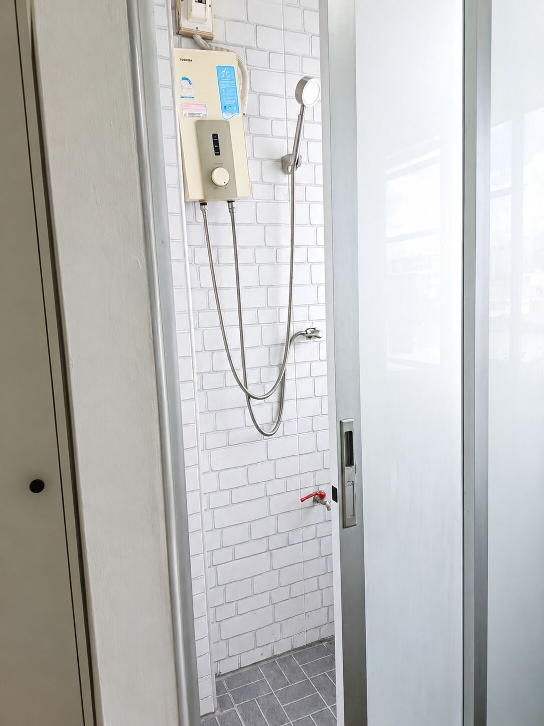 A bathroom with a white brick wall, a handheld showerhead, and a control panel.