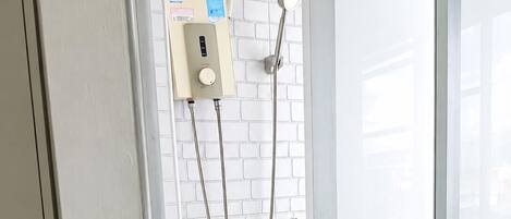 A bathroom with a white brick wall, a handheld showerhead, and a control panel.