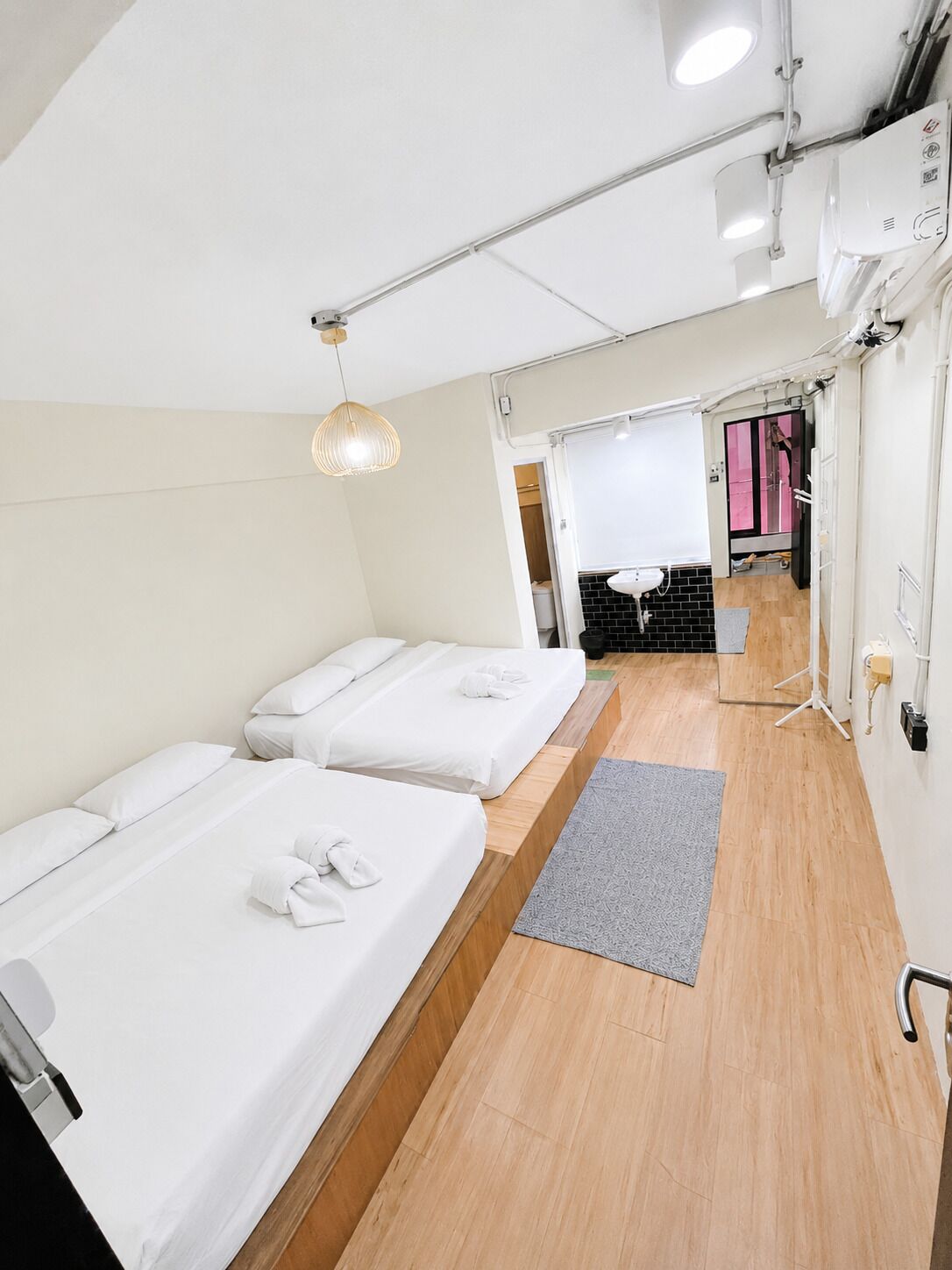 A hotel room with two beds, a small desk, and a bathroom visible through an open door.