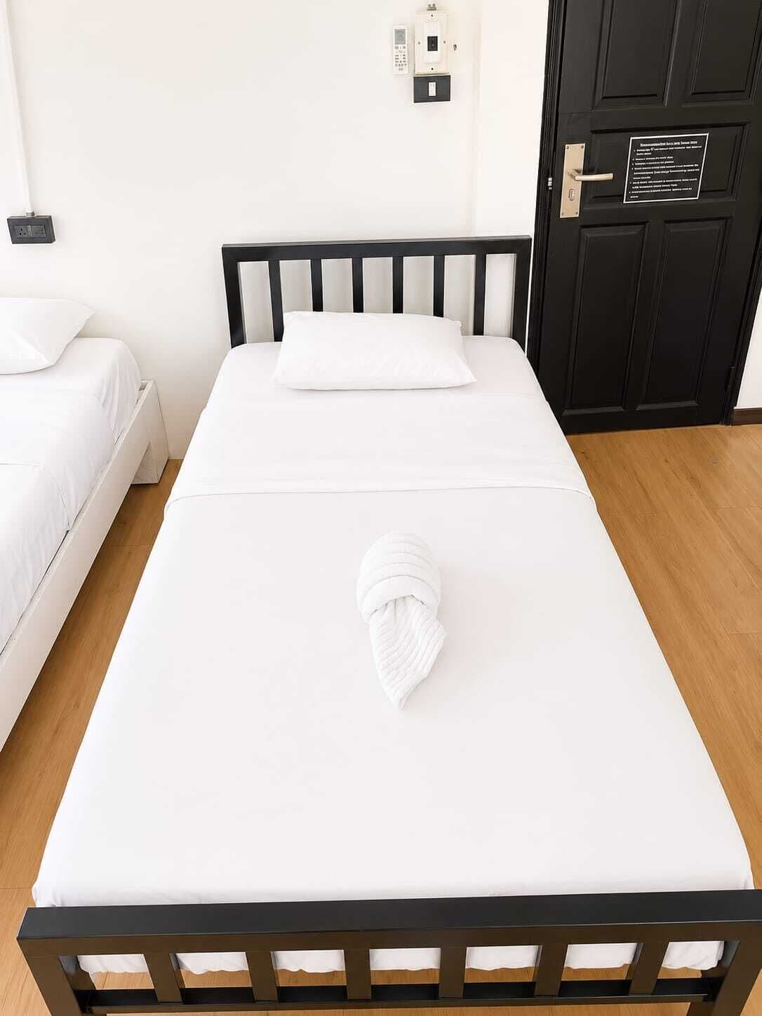 Ein Einzelbett mit weißer Matratze und einem ordentlich gefalteten weißen Handtuch am Fußende.