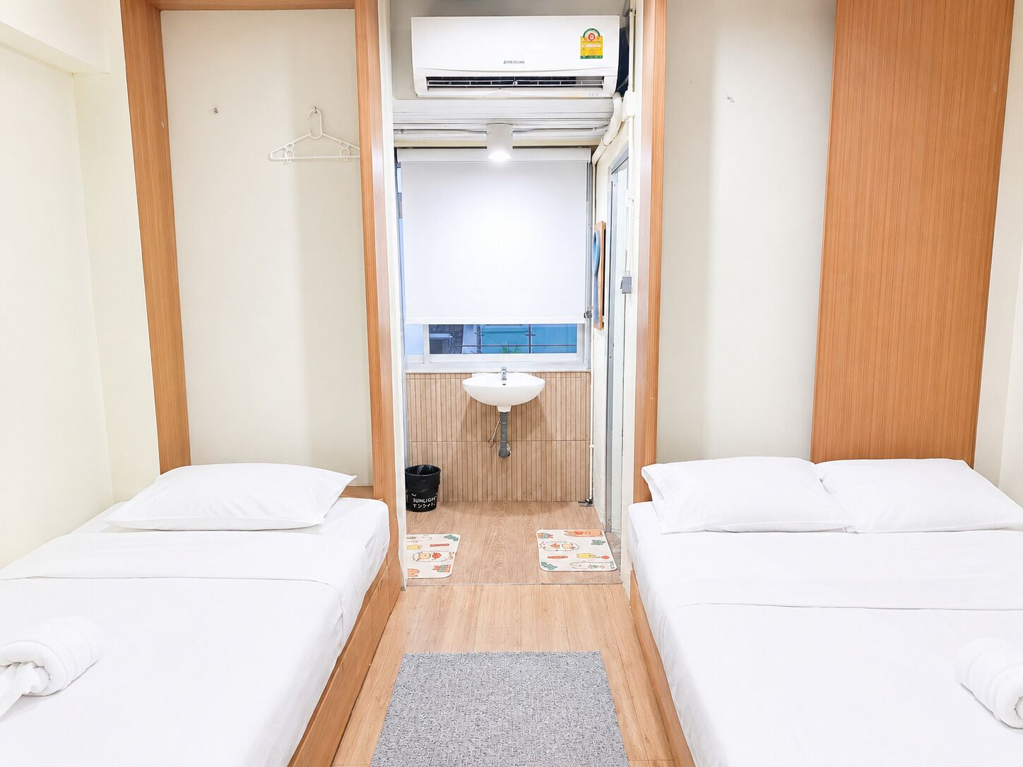 A compact room with two beds, a small bathroom with a sink, and a window.