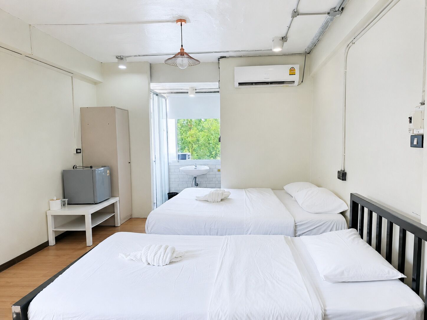 A hotel room with two beds, a desk, a wardrobe, and an air conditioning unit.