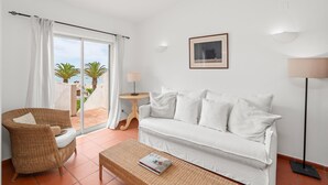 Een witte bank, een rieten stoel en een kleine tafel met een lamp in een kamer met uitzicht op zee.
