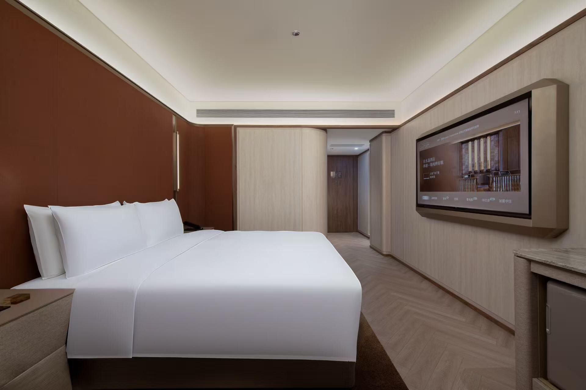 Una habitación de hotel con una cama grande, un televisor montado en la pared y piso de madera.
