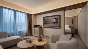 Une chambre d’hôtel moderne équipée d’une grande télévision, d’un canapé, d’une table basse et d’une petite kitchenette.