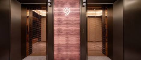 An elevator with a digital display showing the number 9, leading to a room with patterned walls and a bed.
