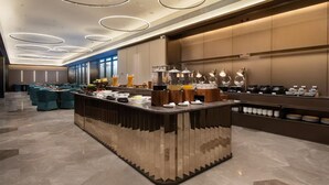 Un hall d’hôtel moderne doté d’un espace buffet central, de différents types de sièges et d’une grande fenêtre laissant entrer la lumière naturelle.