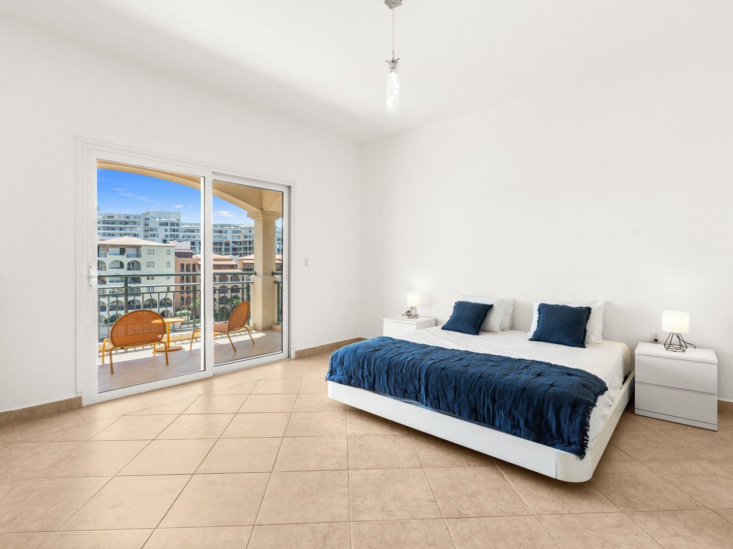 A bedroom with a large bed, two bedside tables, a sliding glass door to a balcony, and a city view.