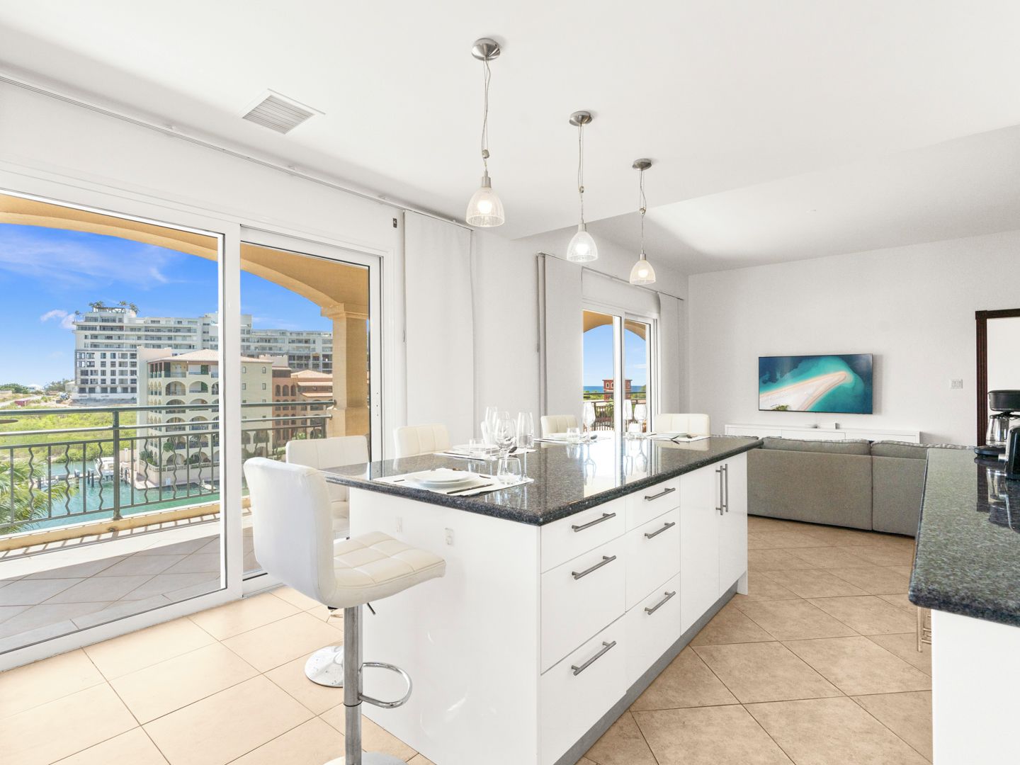 A modern kitchen with a large island, a dining area with a bar stool, and a large window with a view of buildings and a pool.