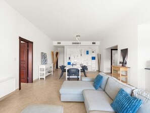 Ein modernes Wohnzimmer mit einer Couch, einem Esstisch mit Stühlen und einer Küche im Hintergrund.