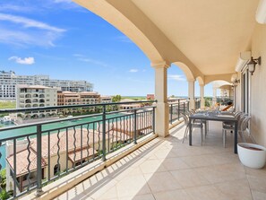 Un balcon donnant sur une piscine et des immeubles, une table avec des chaises et une plante en pot.