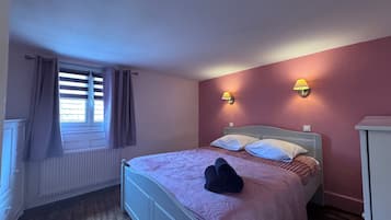 A bedroom with a bed, two wall-mounted lamps, a radiator, and a window with curtains.