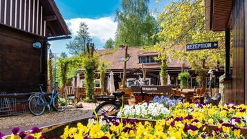 A wooden building with a sign reading 'RECEPTION' and 'BIERGARTEN,' a bicycle, and a flower garden.