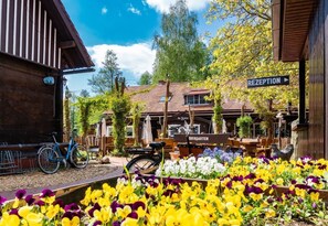 Edificio de madera con un cartel que dice 'RECEPTION' y 'BIERGARTEN', una bicicleta y un jardín de flores.