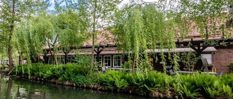 A riverside building with a brick facade, large windows, and outdoor seating by the water.
