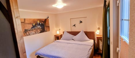 Une chambre à coucher comprenant un lit, deux lampes de chevet, un luminaire fixé au mur, une fenêtre avec des rideaux et un élément décoratif mural.