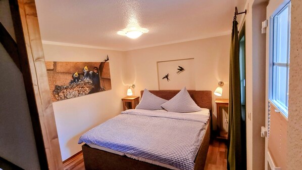 A bedroom with a bed, two bedside lamps, a wall-mounted light fixture, a window with curtains, and a wall decoration.