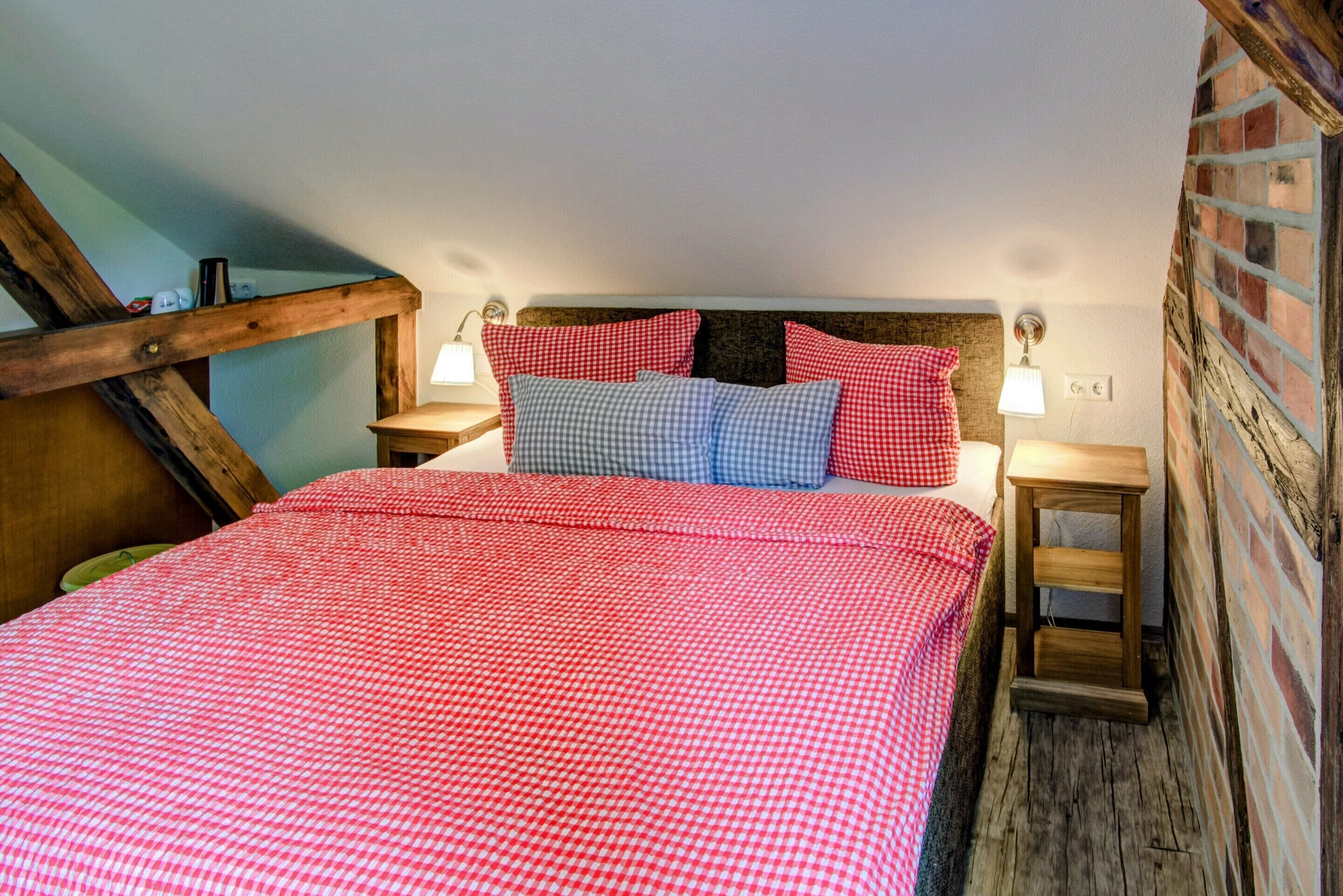 Un dormitorio con colcha de cuadros, cabecero de madera, lámparas de noche y pared de ladrillo.