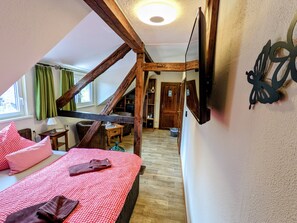 Un dormitorio con techo inclinado, vigas de madera, cama con ropa de cama roja, una mesita y un espejo en la pared.