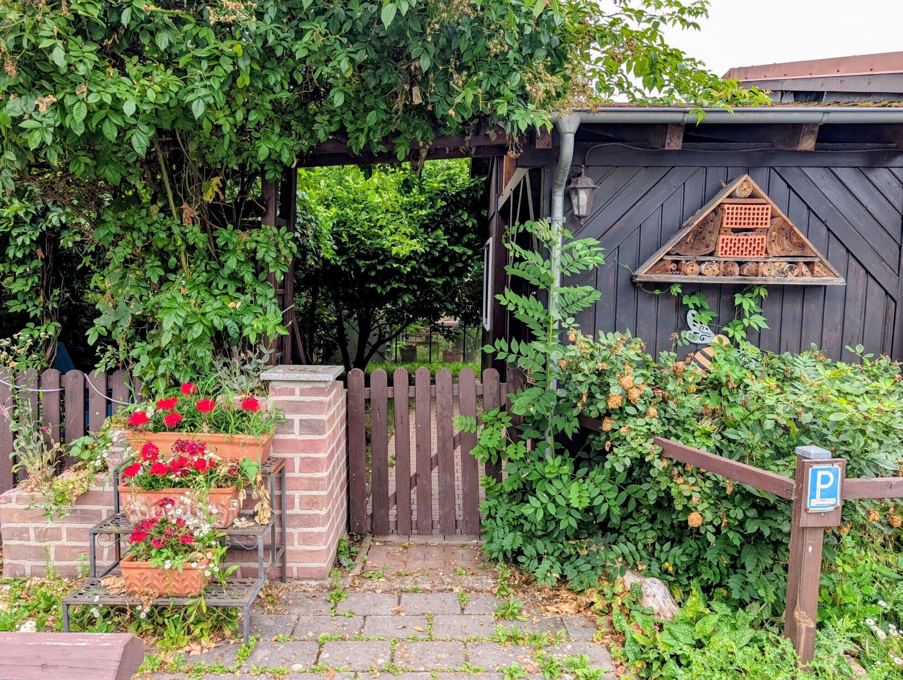 A wooden gate, a brick planter with flowers, and a wooden structure with a triangular window.