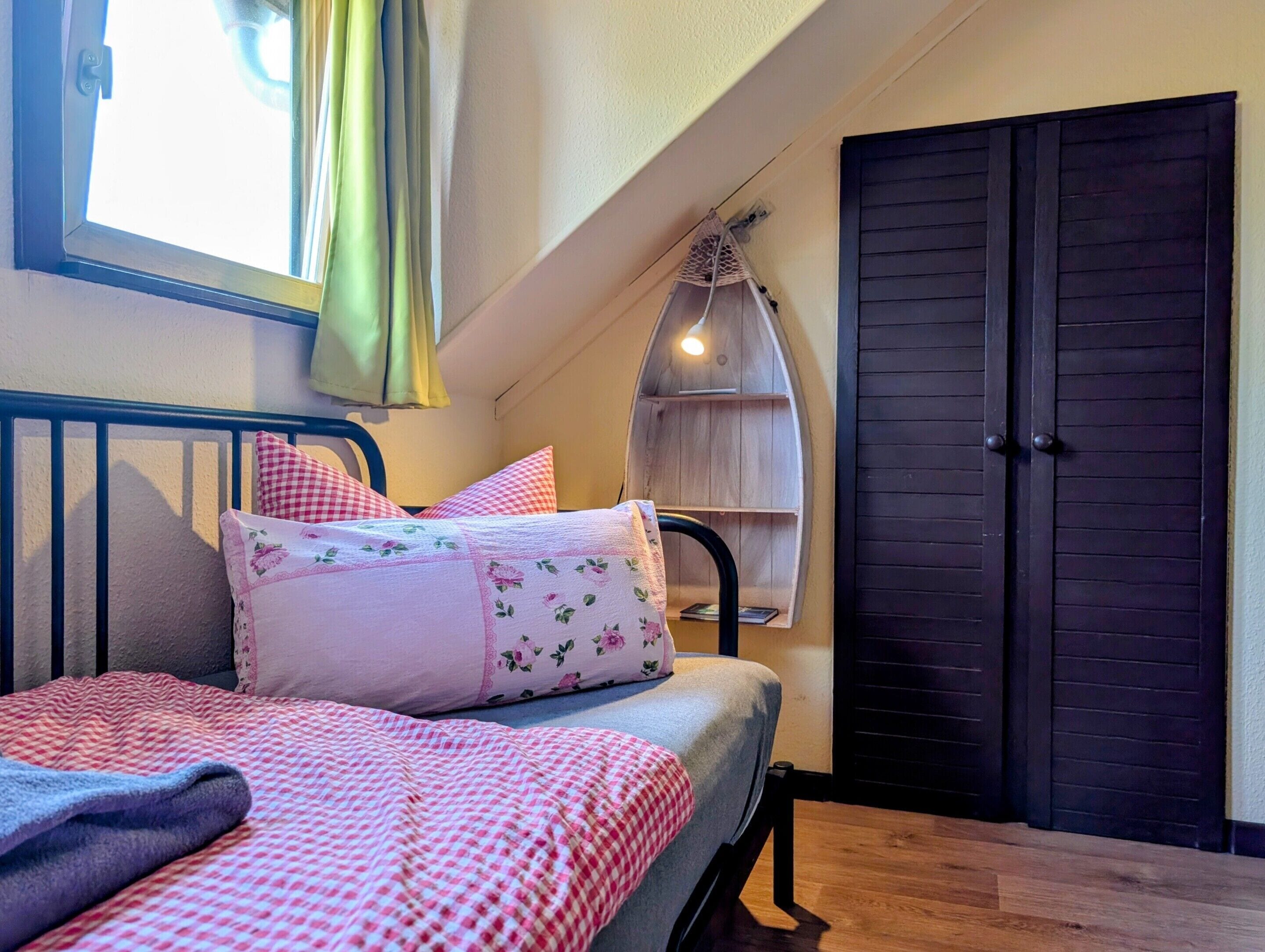 A bedroom with a bed, pillows, a window with curtains, a shelf, and a door.