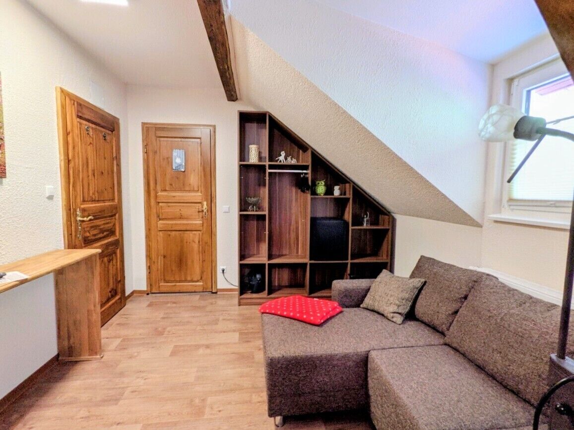 A loft-style room with a wooden staircase, a built-in bookshelf, a sofa, and a window.