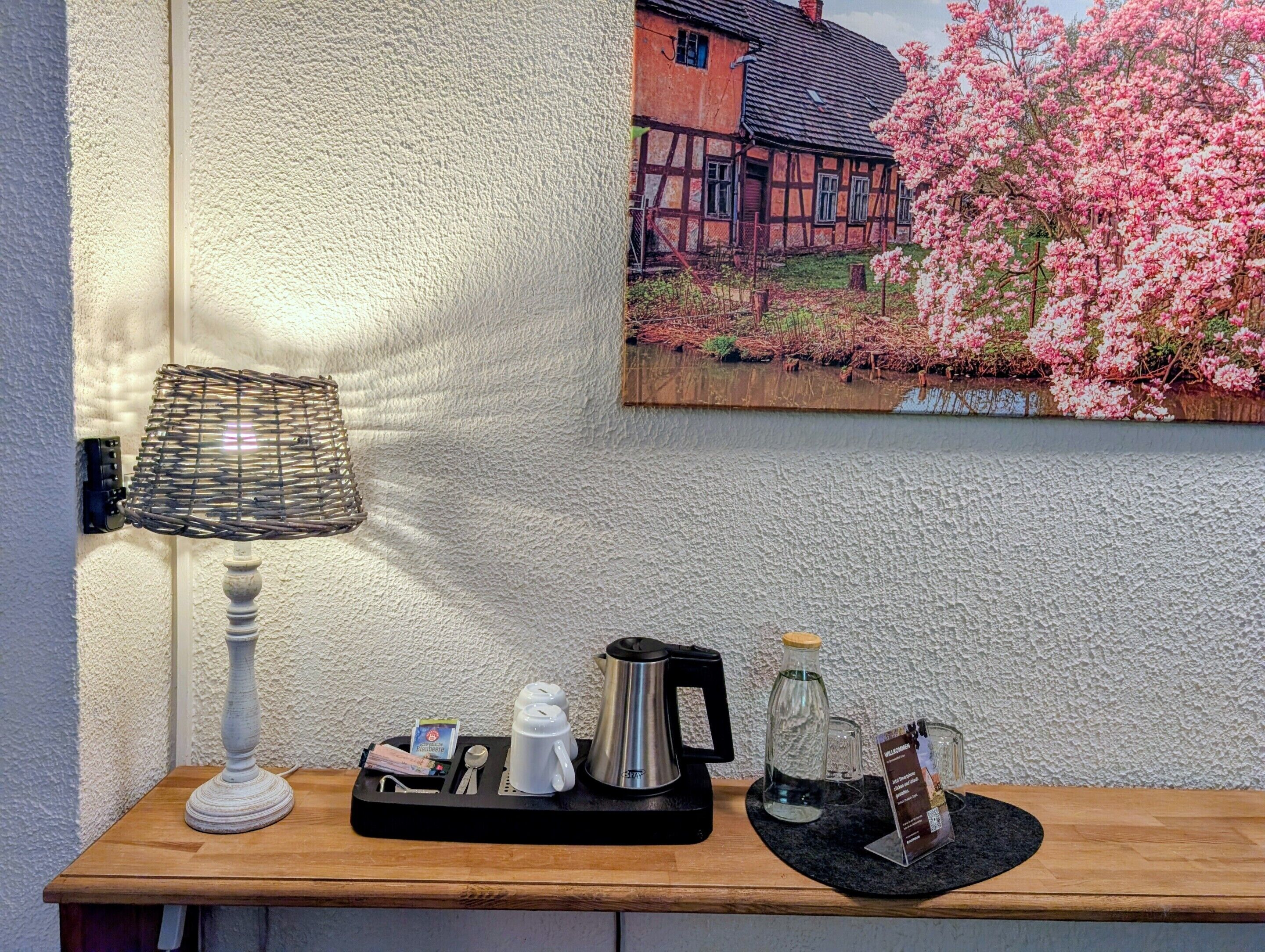 Una estantería de madera con una lámpara, una bandeja con una cafetera, tazas y una botella de vidrio.