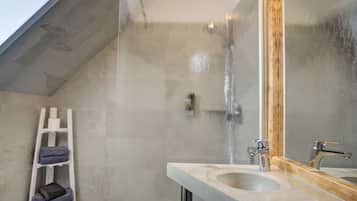 A bathroom with a shower, a sink, a mirror, and a white ladder with towels.